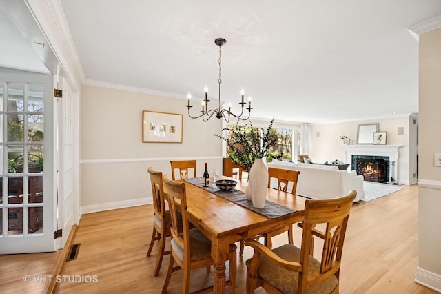 630 Juniper Rd, Glenview, IL 60025 - dining room featuring light wood-style flooring, baseboards, a chandelier, ornamental molding, and a lit fireplace