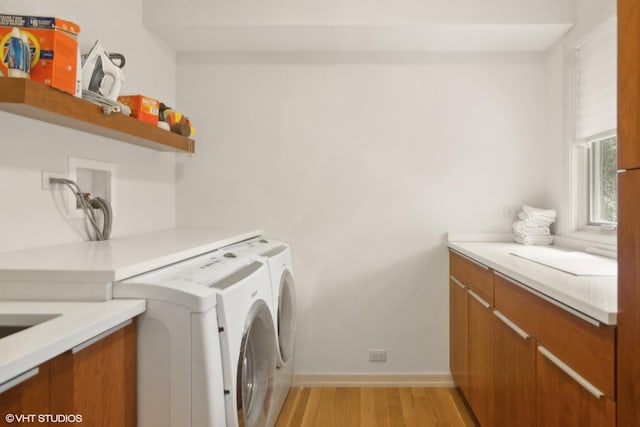 clothes washing area with separate washer and dryer, light wood-style flooring, baseboards, and cabinet space
