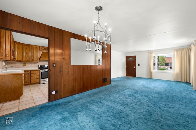 unfurnished dining area with a chandelier, a sink, light carpet, and wooden walls