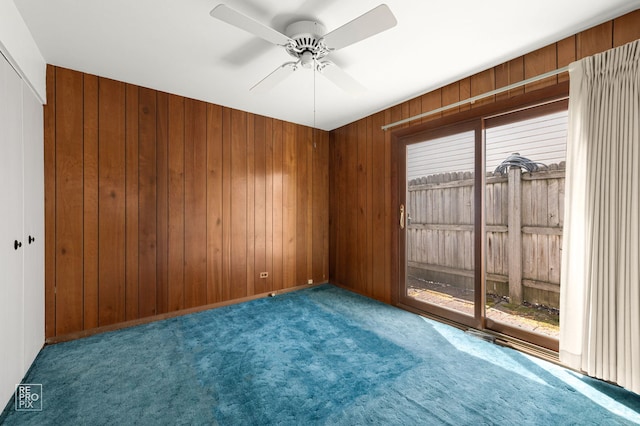 spare room with carpet, wood walls, and ceiling fan