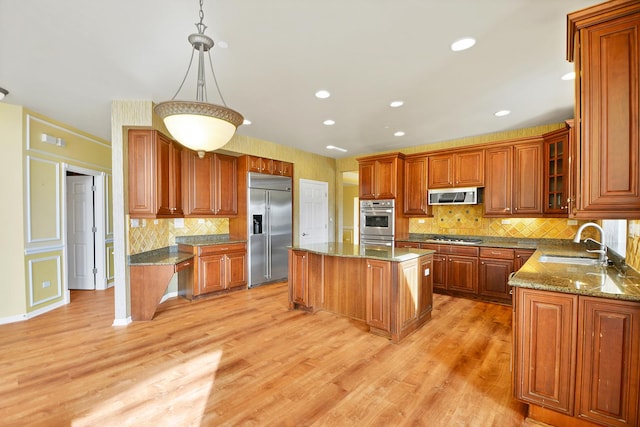 kitchen with appliances with stainless steel finishes, a sink, brown cabinetry, a kitchen island, and light wood-style flooring