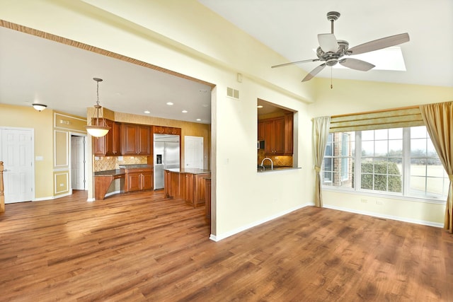 unfurnished living room with ceiling fan, wood finished floors, a sink, baseboards, and vaulted ceiling