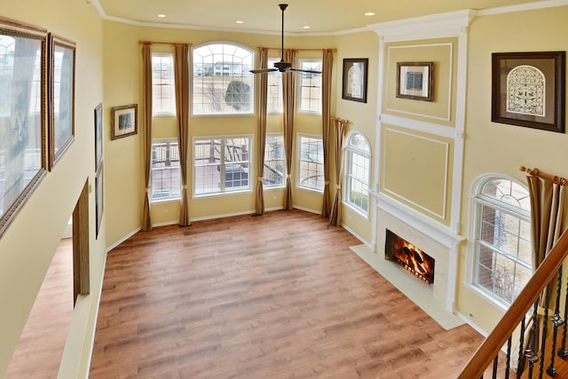 doorway to outside featuring a high end fireplace, crown molding, light wood-style floors, ceiling fan, and baseboards