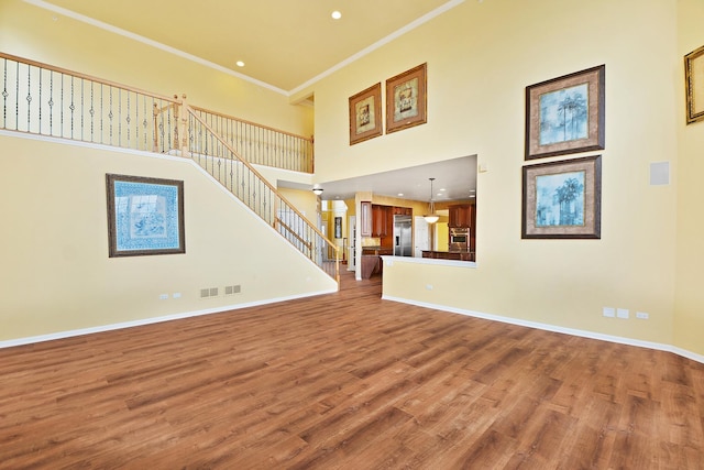 unfurnished living room with wood finished floors, a towering ceiling, crown molding, stairway, and baseboards
