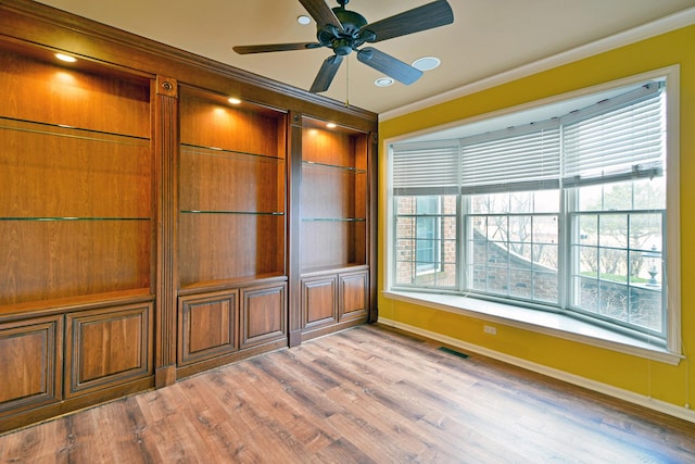 empty room with ornamental molding, wood finished floors, baseboards, and a ceiling fan