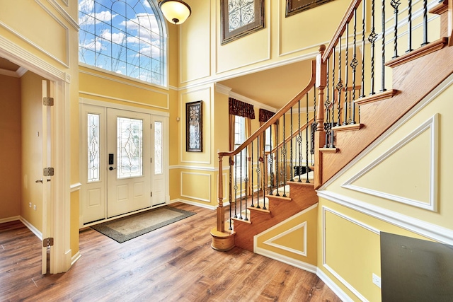 foyer entrance featuring a decorative wall, a high ceiling, wood finished floors, stairs, and ornamental molding