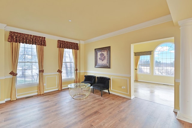 living area with decorative columns, wood finished floors, crown molding, and a wainscoted wall