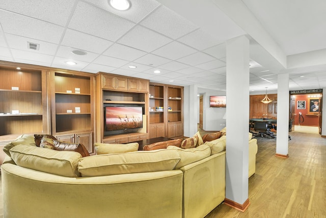 living area featuring a drop ceiling, light wood-style floors, built in shelves, and recessed lighting