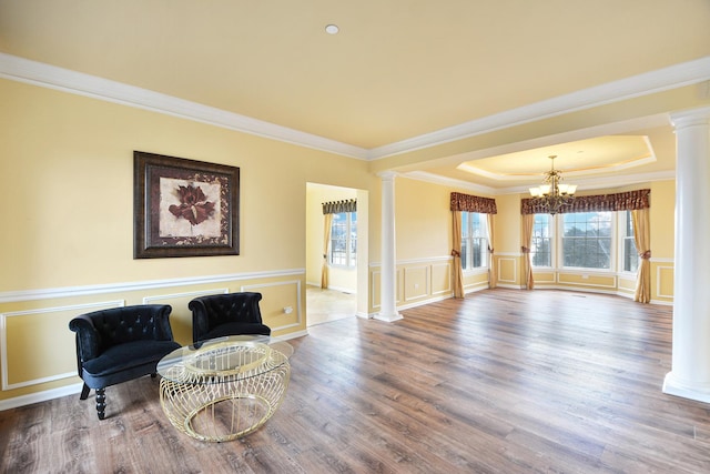 sitting room with ornate columns, a chandelier, wood finished floors, a raised ceiling, and crown molding