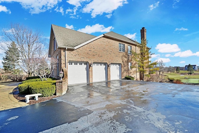 view of property exterior featuring asphalt driveway, a chimney, brick siding, an attached garage, and a shingled roof