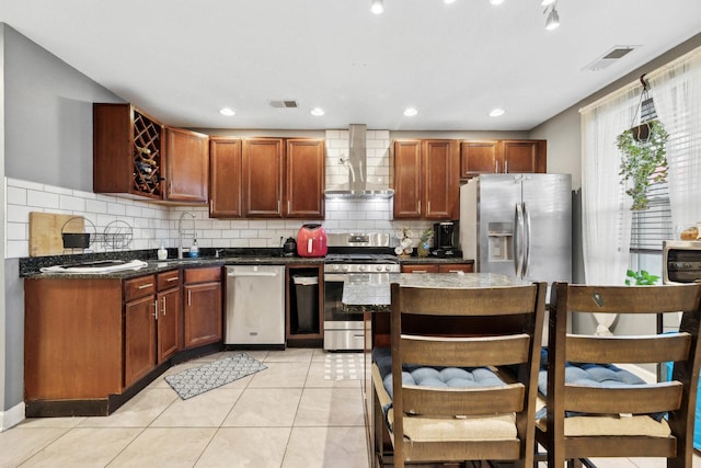 kitchen featuring wall chimney exhaust hood, appliances with stainless steel finishes, a sink, backsplash, and light tile patterned floors