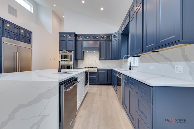 kitchen with a sink, appliances with stainless steel finishes, light wood finished floors, light stone counters, and decorative backsplash