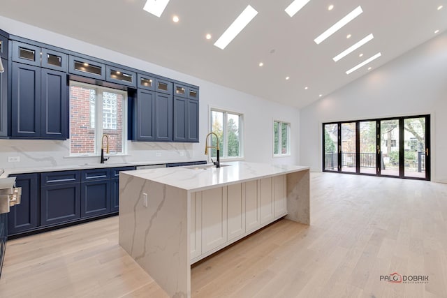 kitchen featuring a sink, an island with sink, high vaulted ceiling, light wood-style floors, and a skylight