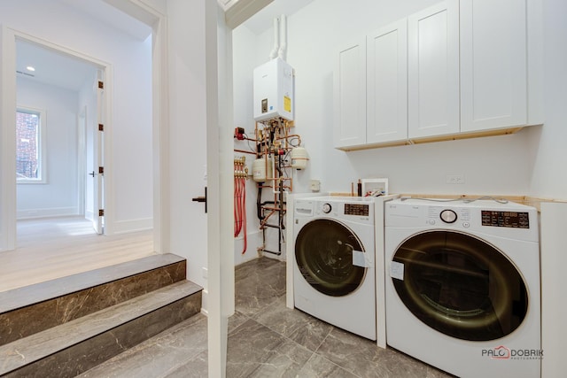 clothes washing area with cabinet space, washer and clothes dryer, water heater, light marble finish flooring, and baseboards