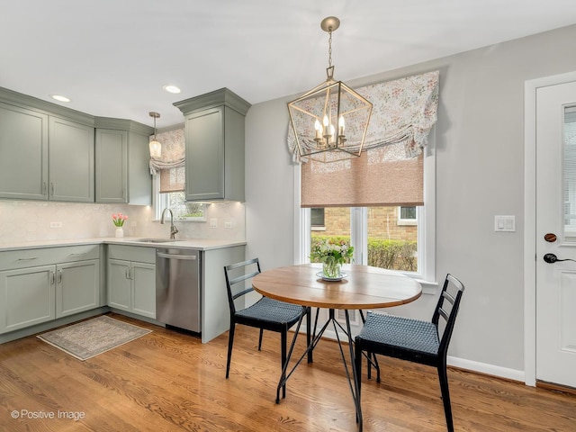 kitchen featuring stainless steel dishwasher, green cabinets, a chandelier, a sink, and backsplash