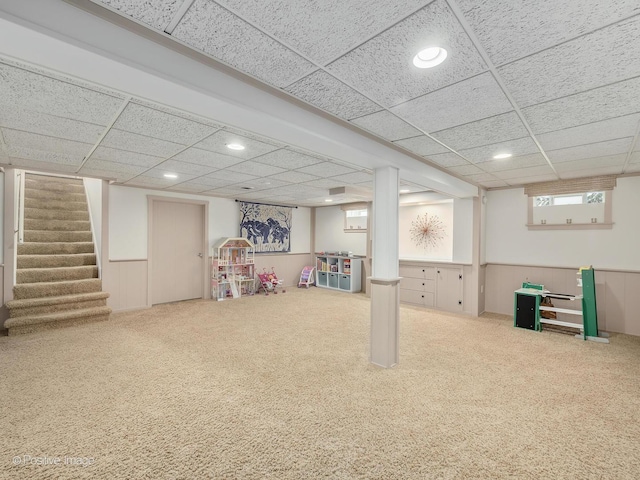 basement featuring a drop ceiling, carpet flooring, recessed lighting, stairs, and wainscoting