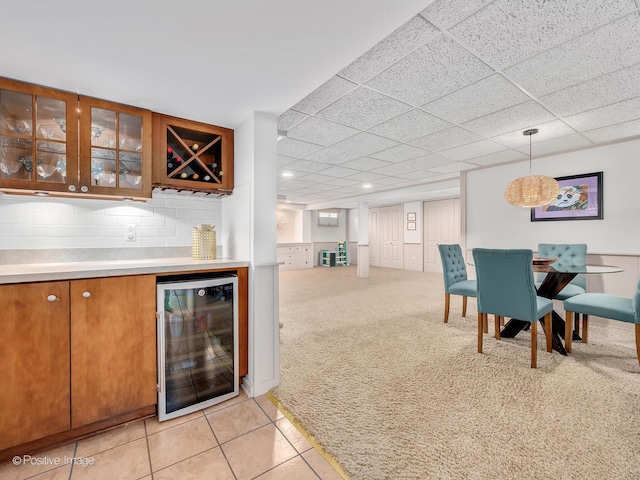 dining room with beverage cooler, a bar, a paneled ceiling, light carpet, and light tile patterned floors