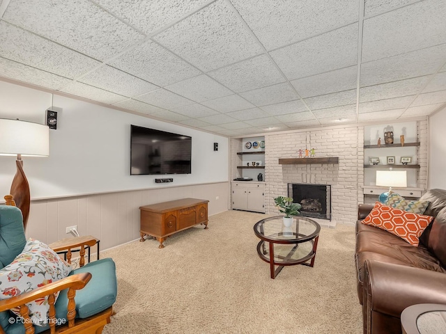 living area featuring built in features, a fireplace, carpet flooring, wainscoting, and a paneled ceiling