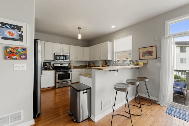16030 Tahoe Ln, Crest Hill, IL 60403 - kitchen featuring stainless steel appliances, a kitchen bar, wood finished floors, white cabinets, and recessed lighting