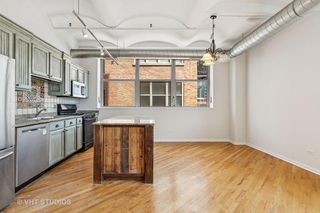 kitchen with stainless steel appliances, light wood finished floors, a sink, and baseboards