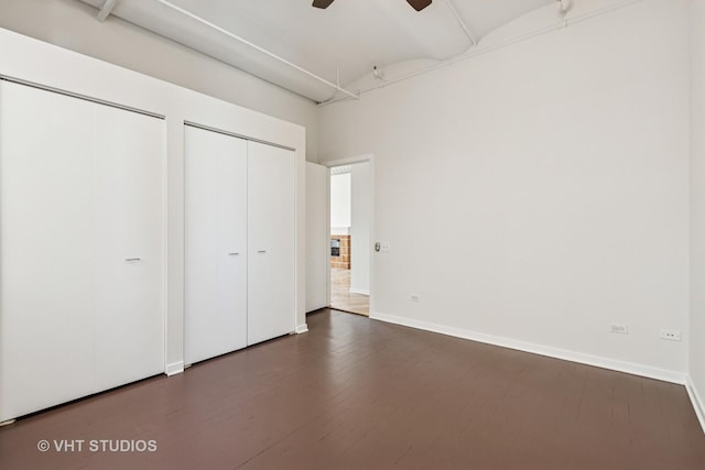 unfurnished bedroom featuring dark wood-style flooring, baseboards, a ceiling fan, and multiple closets