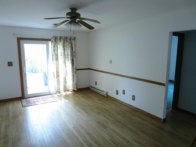 spare room with a baseboard heating unit, a ceiling fan, wood finished floors, and baseboards