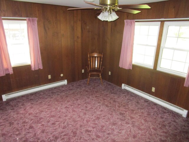 carpeted empty room featuring a baseboard heating unit, baseboard heating, healthy amount of natural light, wooden walls, and ceiling fan