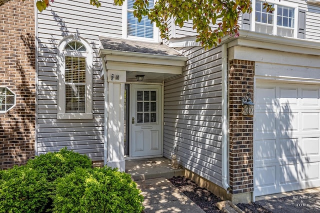 view of exterior entry featuring an attached garage and brick siding