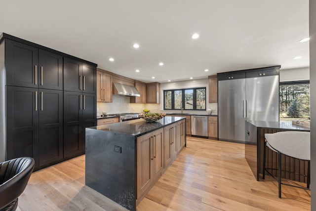 kitchen with appliances with stainless steel finishes, wall chimney exhaust hood, healthy amount of natural light, tasteful backsplash, and recessed lighting