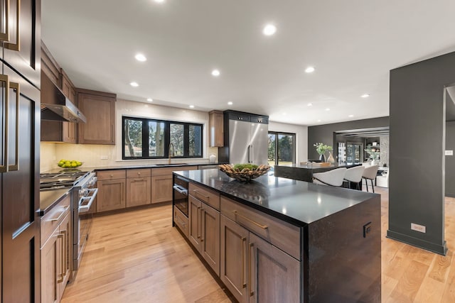 kitchen with high quality appliances, a sink, wall chimney range hood, light wood-style flooring, and recessed lighting