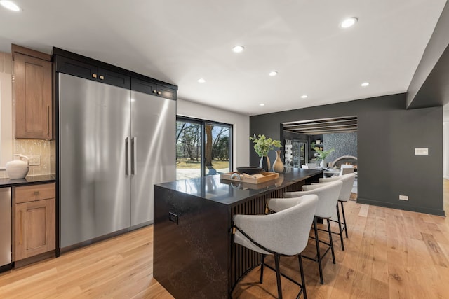 kitchen featuring high end fridge, dark countertops, recessed lighting, light wood-style flooring, and a center island