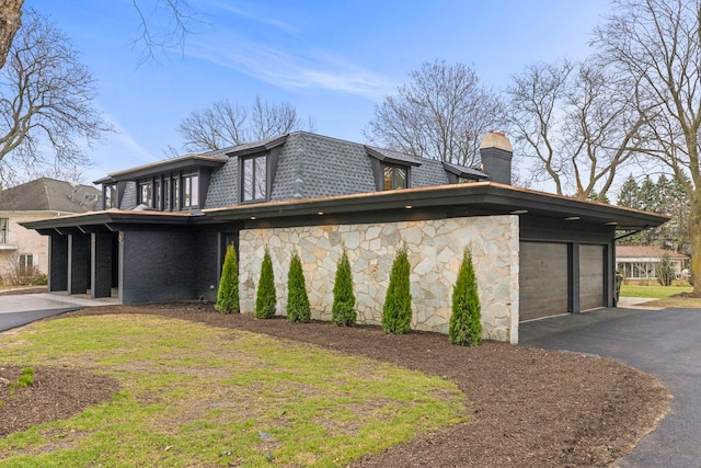 view of property exterior featuring a chimney, a garage, mansard roof, a shingled roof, and stone siding