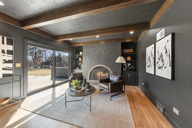 living room featuring wood finished floors, beam ceiling, a textured ceiling, built in shelves, and baseboards