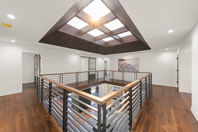 hall featuring a raised ceiling, baseboards, a skylight, wood finished floors, and recessed lighting