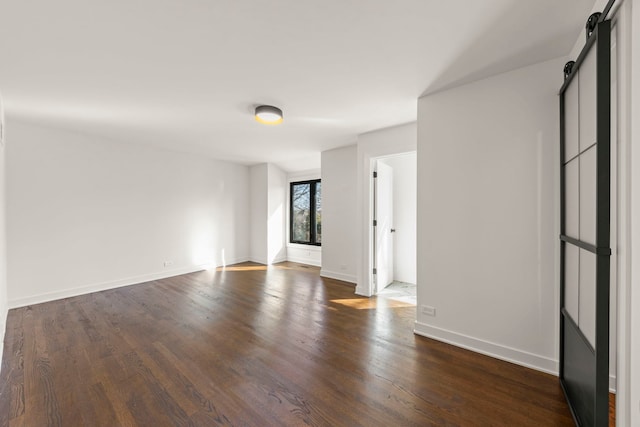 spare room featuring a barn door, dark wood finished floors, and baseboards