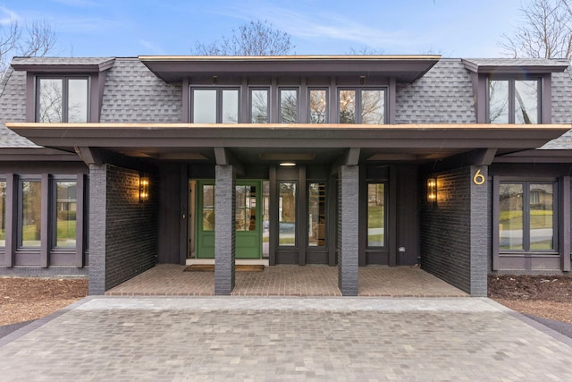 view of exterior entry featuring mansard roof, a shingled roof, and brick siding