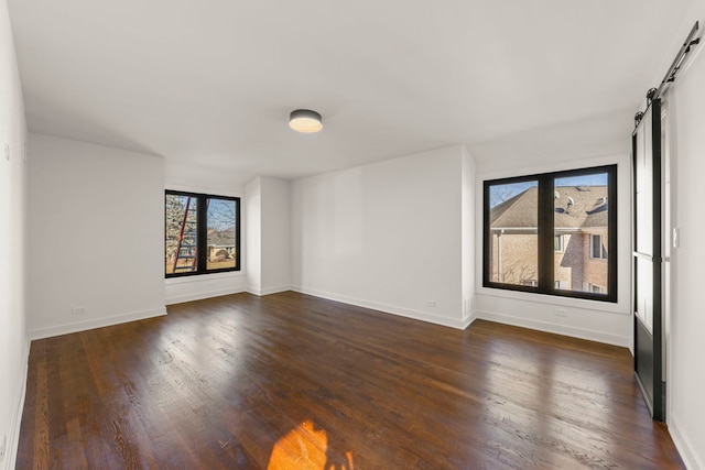 spare room with a barn door, dark wood-style floors, and baseboards
