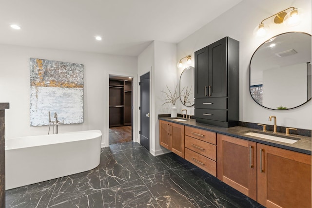 bathroom with marble tiled floors, double vanity, recessed lighting, a freestanding tub, and a walk in closet