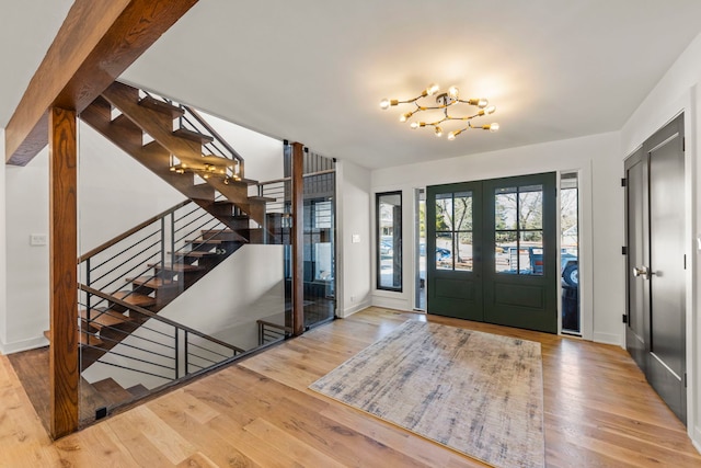 entrance foyer with french doors, wood finished floors, baseboards, a chandelier, and stairway