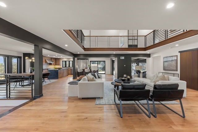 living room with light wood-type flooring, plenty of natural light, a towering ceiling, a chandelier, and recessed lighting