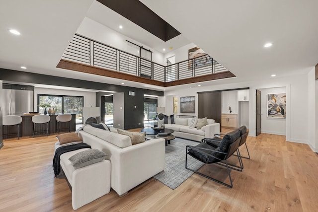 living room featuring a high ceiling, light wood-style flooring, recessed lighting, and baseboards