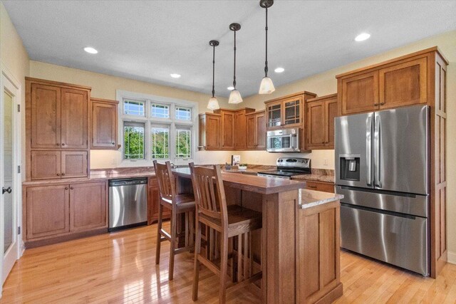 2297 Deer Ridge Ct, Carlock, IL 61725 - kitchen featuring stainless steel appliances, brown cabinets, a kitchen island, light wood-style floors, and hanging light fixtures