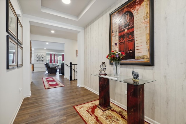 hallway with an upstairs landing, dark wood-type flooring, baseboards, recessed lighting, and a raised ceiling