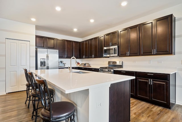 kitchen featuring stainless steel appliances, a sink, a breakfast bar area, light wood-style flooring, and an island with sink