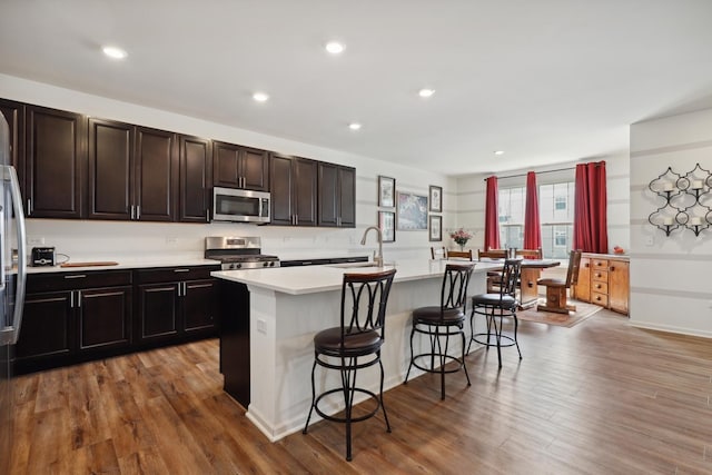 kitchen featuring stainless steel appliances, a sink, a kitchen bar, light countertops, and an island with sink