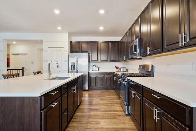 kitchen with stainless steel appliances, a sink, light wood-style flooring, dark brown cabinetry, and light countertops