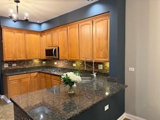 kitchen with stainless steel microwave, decorative backsplash, baseboards, a sink, and a peninsula