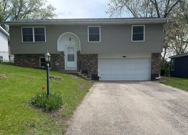 split foyer home with brick siding, an attached garage, asphalt driveway, and a front lawn