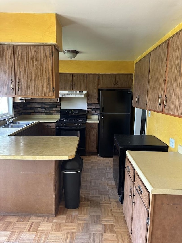 kitchen featuring black appliances, under cabinet range hood, a peninsula, light countertops, and a sink