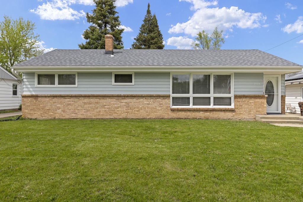 back of house featuring brick siding, a yard, a chimney, and a shingled roof
